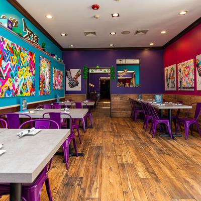 Interior with colorful walls, tables, purple chairs, and vibrant wall art.