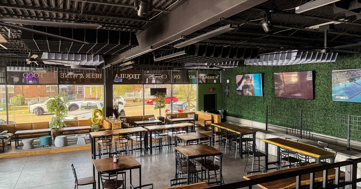 Interior with wooden tables, metal chairs, TVs on a plant-textured wall, and large windows