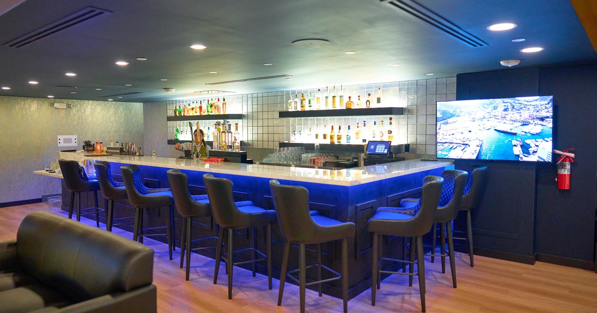 Modern blue-lit bar - liquor shelves, upholstered stools, a TV.
