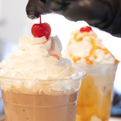 Milkshake topped with whipped cream, being garnished with a cherry.