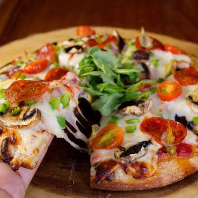 A hand taking a slice of pepperoni pizza with cheese, mushrooms, and arugula.