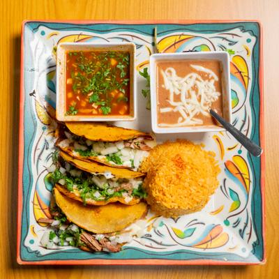Birria tacos served with consomme, rice, and refried beans on a colorful plate.