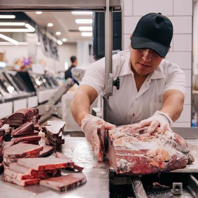 A market employee cuts meat at a counter.