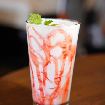 Sweet lassi served in a glass drizzled with syrup, garnished with mint.
