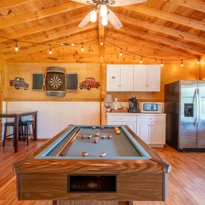 Wooden cabin interior with a bumper table, a dart board, and a kitchenette.