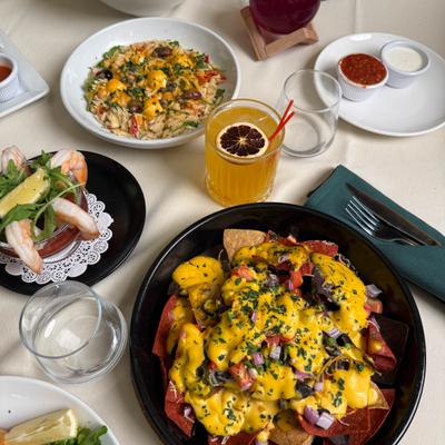 Nachos with cheese, shrimp cocktail, and pasta salad with colorful cocktails on a table.