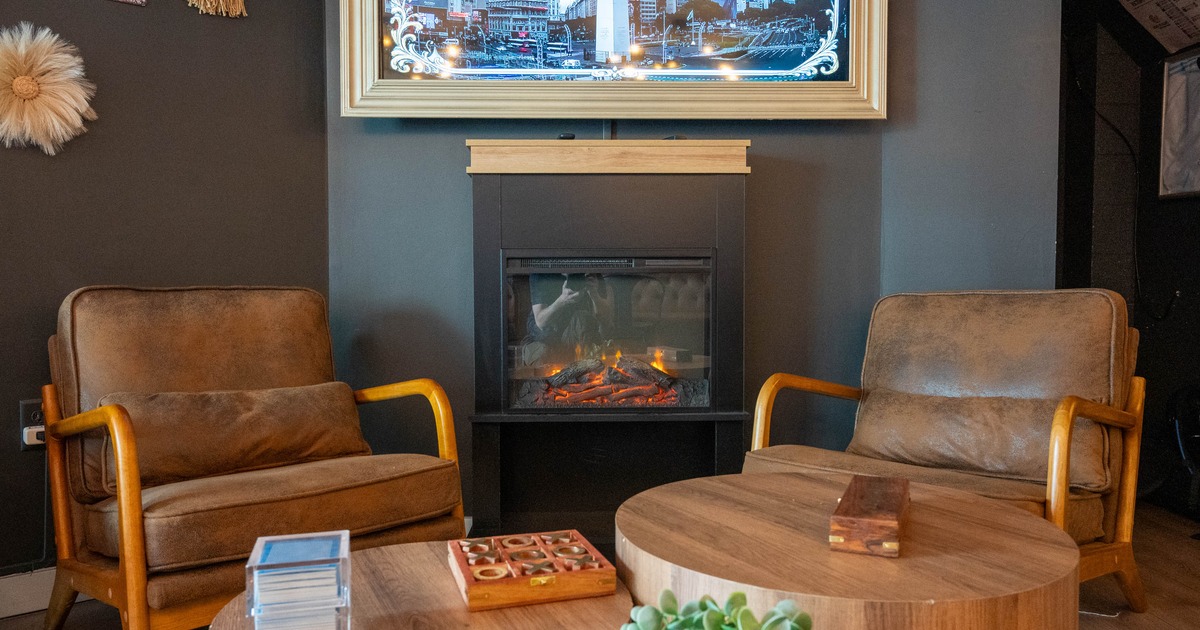A cozy seating area with armchairs, a fireplace, and wooden tables.