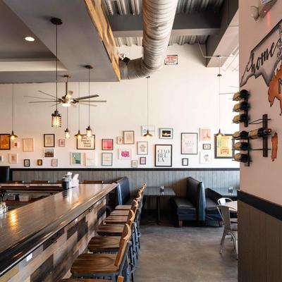 Bar counter and chairs, dining booths arranged by a wall with framed pictures.