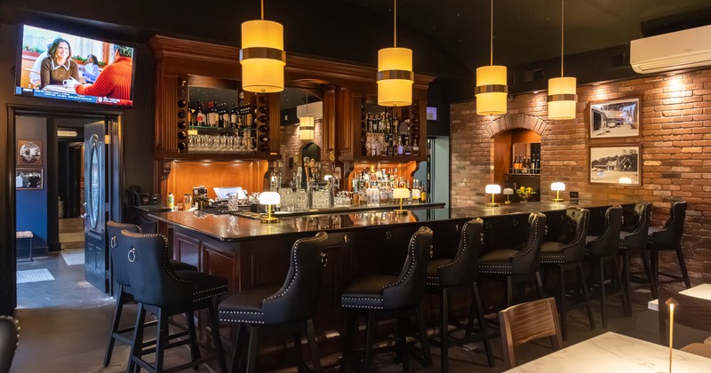 A cozy bar with wooden decor, black bar stools, pendant lights and a flat-screen TV on the wall