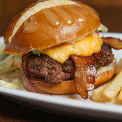 Bacon cheeseburger on a brioche bun served with fries, close-up.