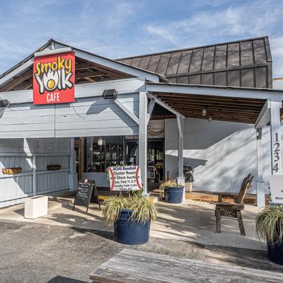 Exterior of Smoky Yolk Cafe featuring a sign, promotional poster, and potted plants