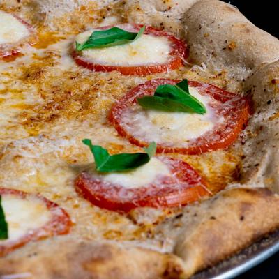 Margherita pizza with sliced fresh tomato, mozzarella, and basil leaves.
