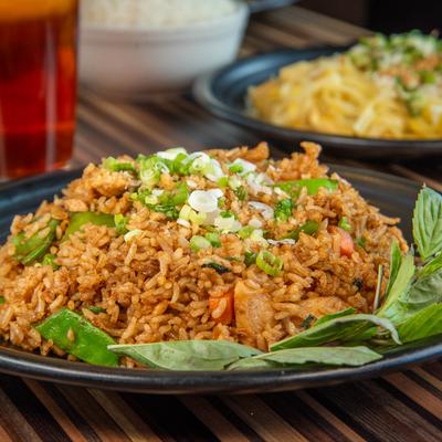 Thai fried rice with vegetables and herbs on a black plate.