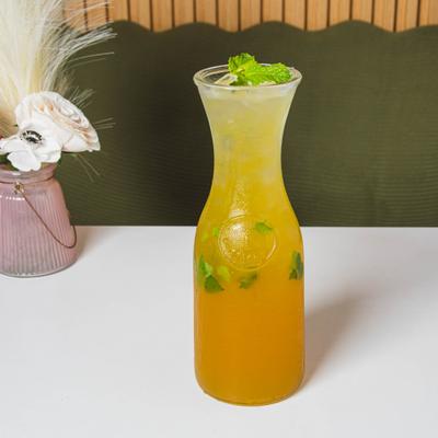 A tall glass carafe with Jasmine kumquat tea sits on a table.