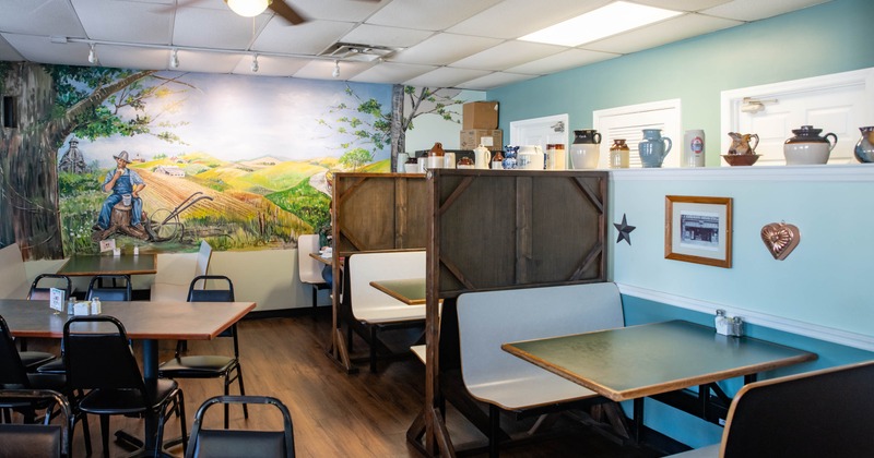 Interior of a café with rustic décor, tables, and a mural of a countryside