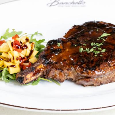 Bone-in ribeye steak with glossy glaze and fresh fruit and arugula side.