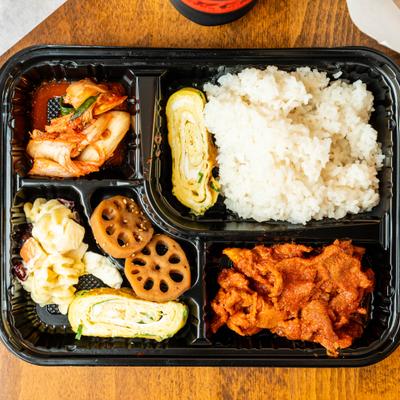 Bento box with spicy pork, rice, kimchi, egg roll and and seasoned lotus root.