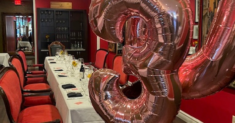 Interior, a table set for dining in a celebration room decorated with rose gold number balloons