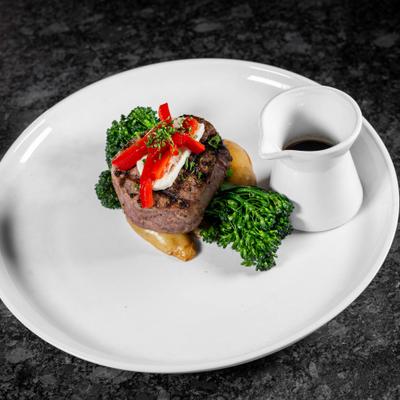 Filet mignon topped with cheese and red bell pepper strips, served with vegetables and sauce.