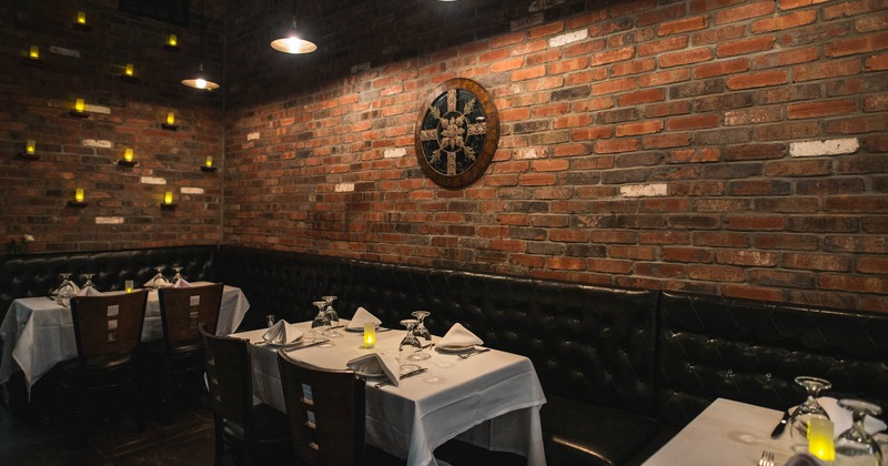 Set dining tables and high back leather seating by brick walls, wall decoration and candle lights