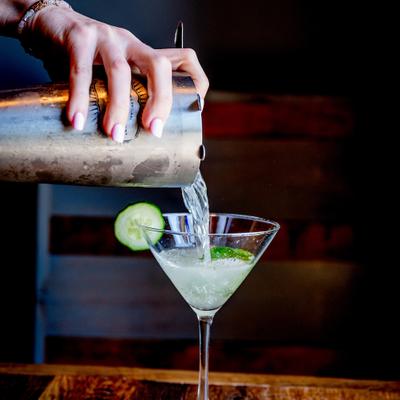 A bartender pours a  cocktail into a classic martini glass.