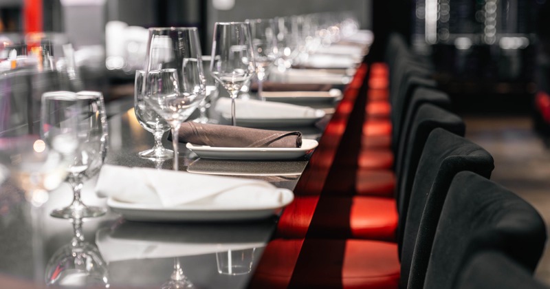 Elegant restaurant setting with a long table with wine glasses, white plates, and brown napkins