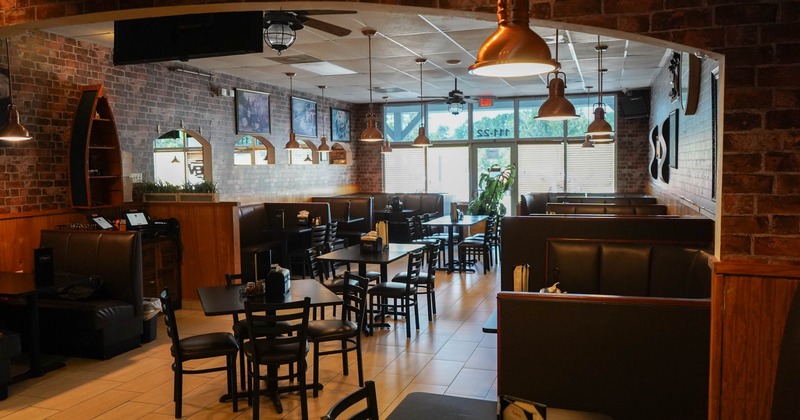 Interior of a restaurant featuring exposed brick walls, wooden and leather seating, pendant lights, and large windows