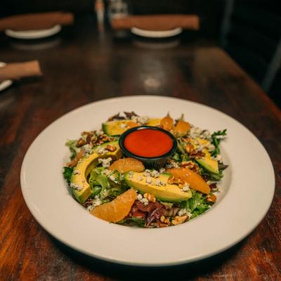 A salad with lettuce, walnuts, blue cheese, orange and avocado, served with a red dressing.