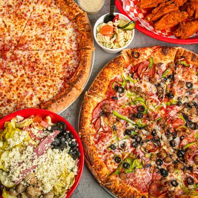 Overhead view of cheese and supreme pizzas  with wings, pasta salad, and antipasto bowls.