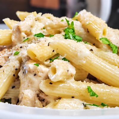 Penne pasta with creamy sauce, meat and chopped herbs in a white bowl..