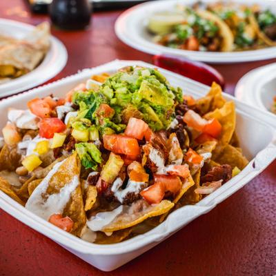 Nachos topped with meat, beans guacamole, diced tomatoes, and a white sauce.