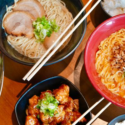 Spread of Japanese dishes featuring two ramen bowls, gyoza, and fried chicken bites.