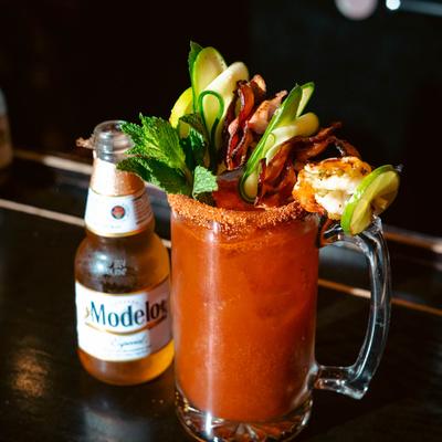 Michelada with rich garnish stands by a bottle of Mexican beer.