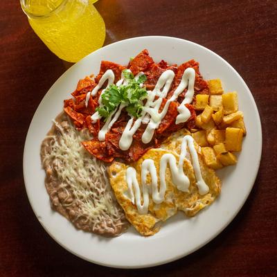 Fried eggs, tortilla chips in red salsa, potatoes, and refried beans.