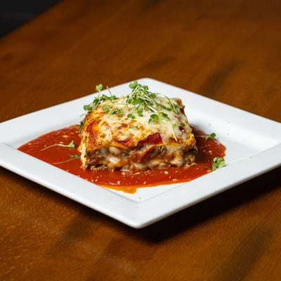 Lasagna in tomato sauce, garnished with fresh microgreen.