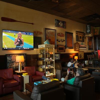 Cozy lounge featuring leather armchairs, decorated walls, and a TV broadcasting a sports program.