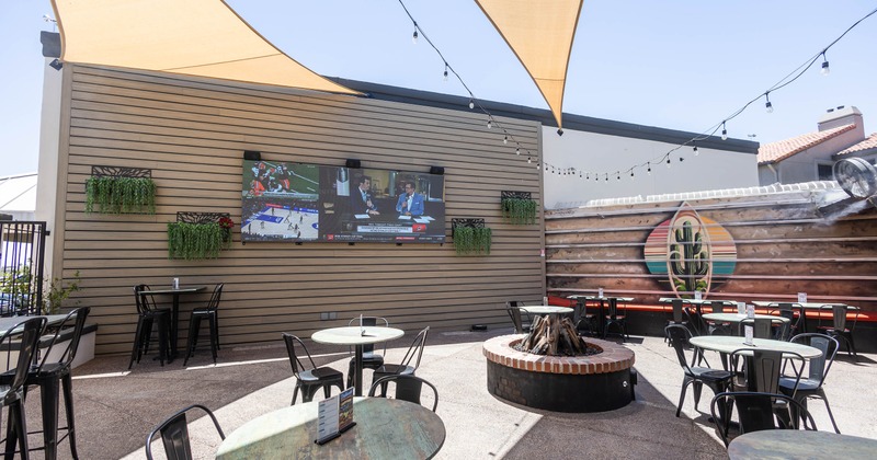 Outdoor patio with round tables and chairs, shaded by large triangular sails