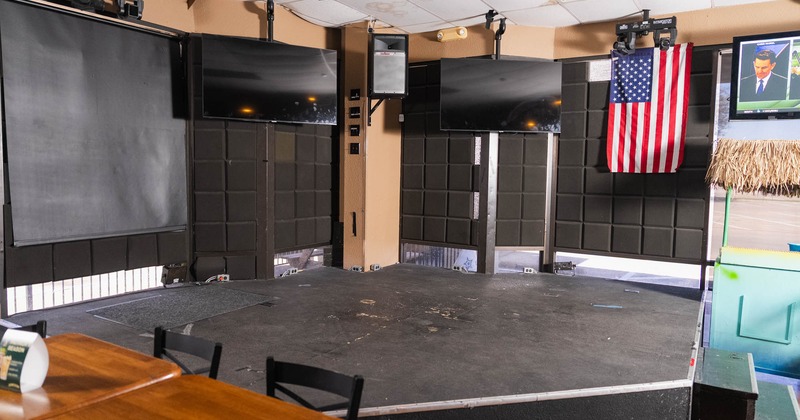 An empty stage featuring two large screens, an American flag, and a dining table