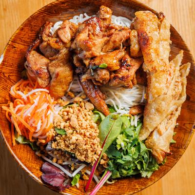 Plate with grilled pork, egg rolls, rice, pickled carrots, rice noodles, lettuce