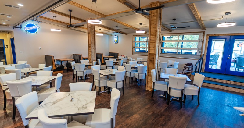 Dining area with marble tables, white chairs, wooden flooring and blue doors