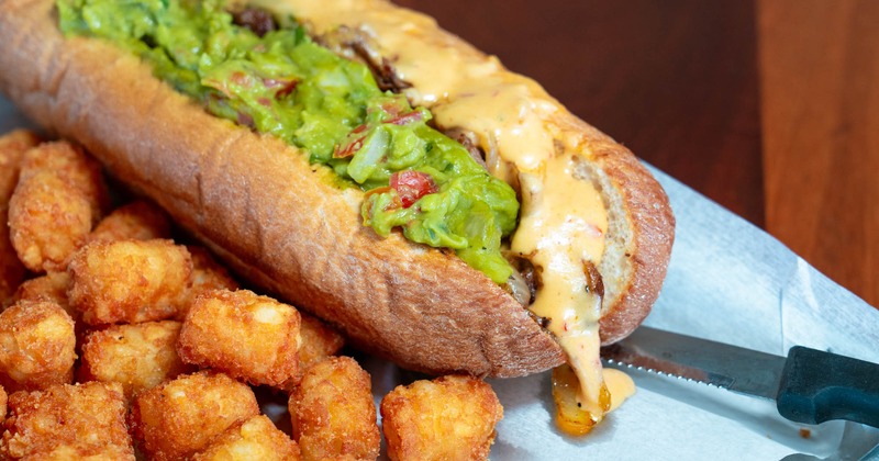 San Diego cheesesteak sandwich with a side of tots, close up