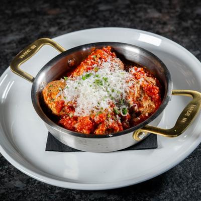 Meatballs in tomato sauce topped with melted cheese and fresh herbs.