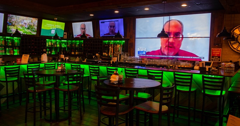 Seating area with tables, chairs, a bar in the back with few TV screens