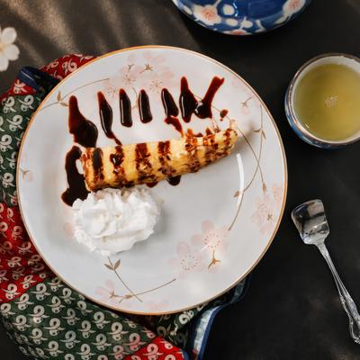 A slice of cheesecake with chocolate drizzle, whipped cream, and green tea.