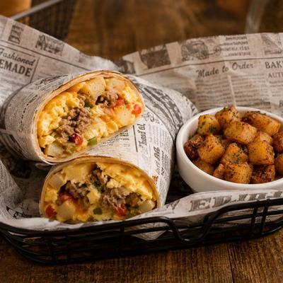 Breakfast burrito wrapped in newspaper-style parchment paper and served with potatoes.