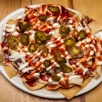 Loaded BBQ pulled pork nachos topped with cheese, jalapenos, and white crema.