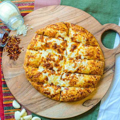 Cheesy garlic bread on a wooden board served with Parmesan, chili flakes, and garlic cloves.