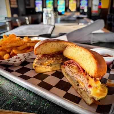 Burger with bacon and cheese served with seasoned fries on metal tray.