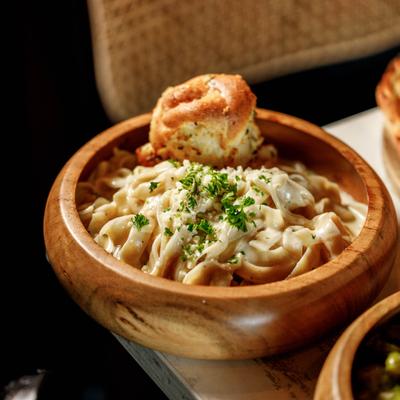 Alfredo pasta served in a wooden bowl with garlic bread.