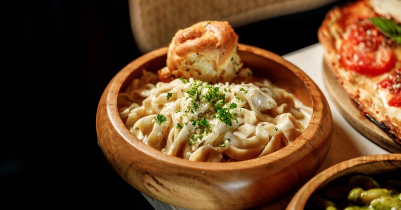 A wooden bowl of Alfredo pasta and garlic bread